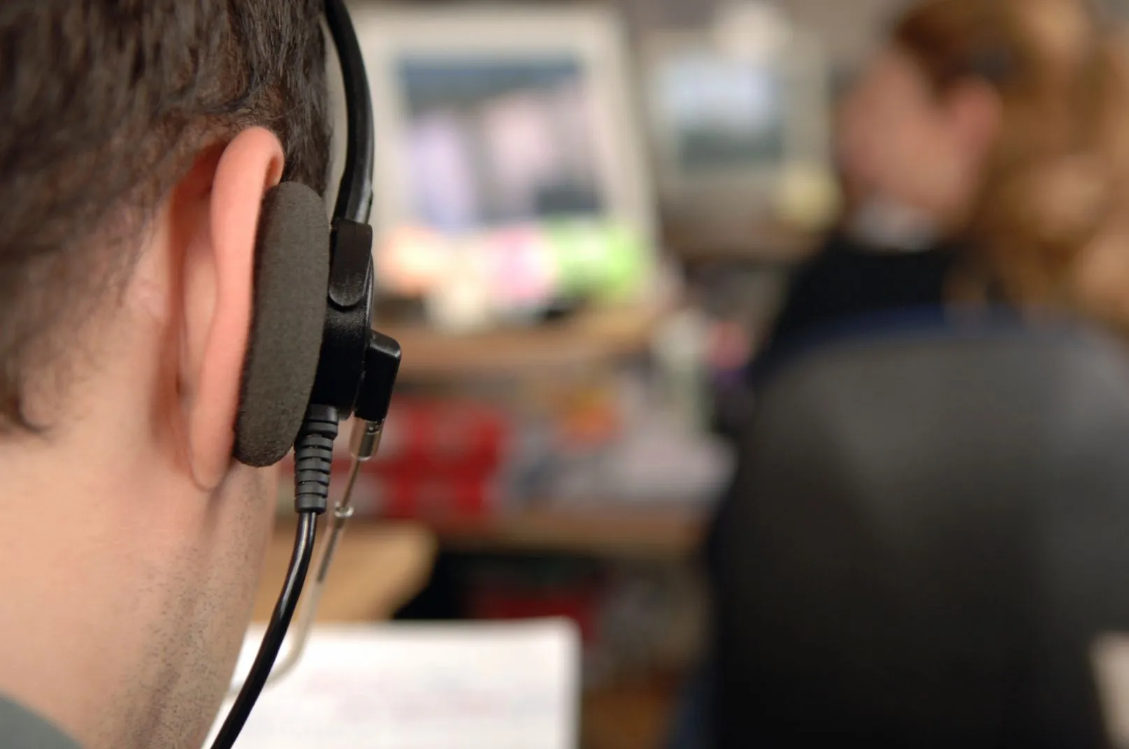 Call-center operator wearing a headset with another agent working in the background