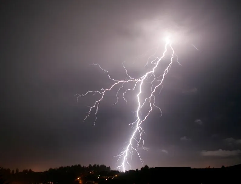 Lightning strike over dark storm clouds above a distant town