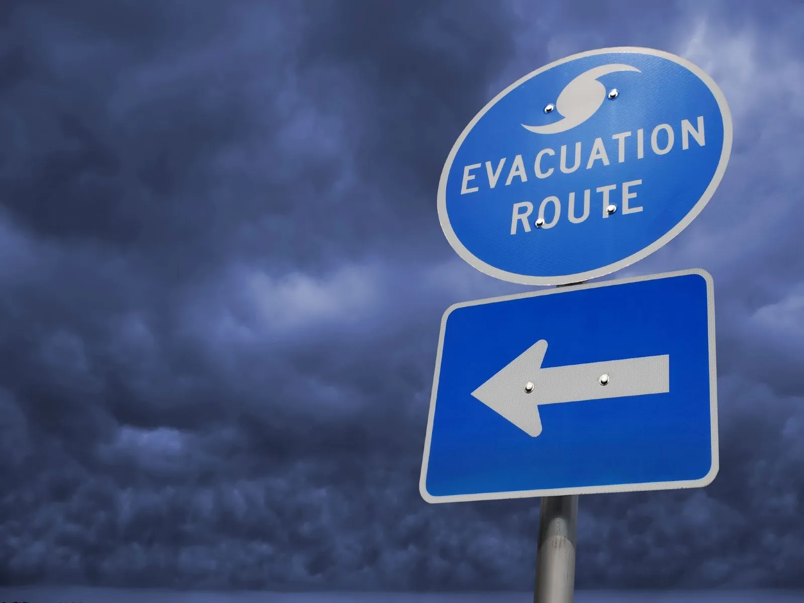 Blue hurricane evacuation route sign beneath dark storm clouds